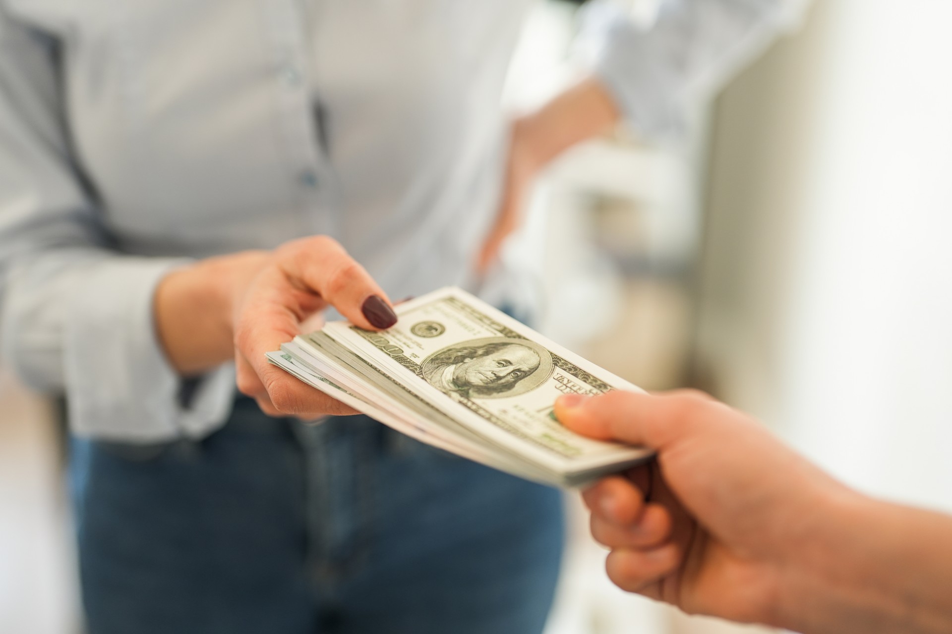 Close-up of woman handing stack of dollars to other person. Getting royalty money that is earned from music, beats, instrumental, lyrics or loops.